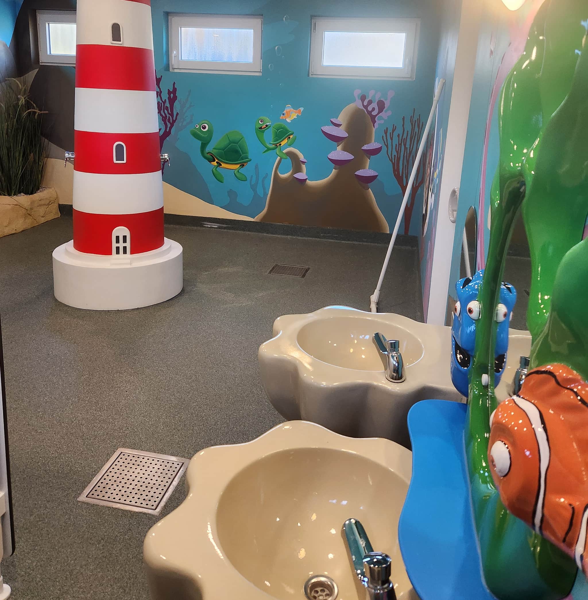 Kinderbad Ein farbenfrohes Kinderbad mit Meeresthemen, einem rot-weißen Leuchtturm, Meerestieren und ungewöhnlich geformten Waschbecken.
